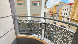 A balcony with a patterned railing, a tiled floor, and a view of adjacent buildings and a street. - Elite Holiday Homes - Luxury & Centric Flat (Tangier)