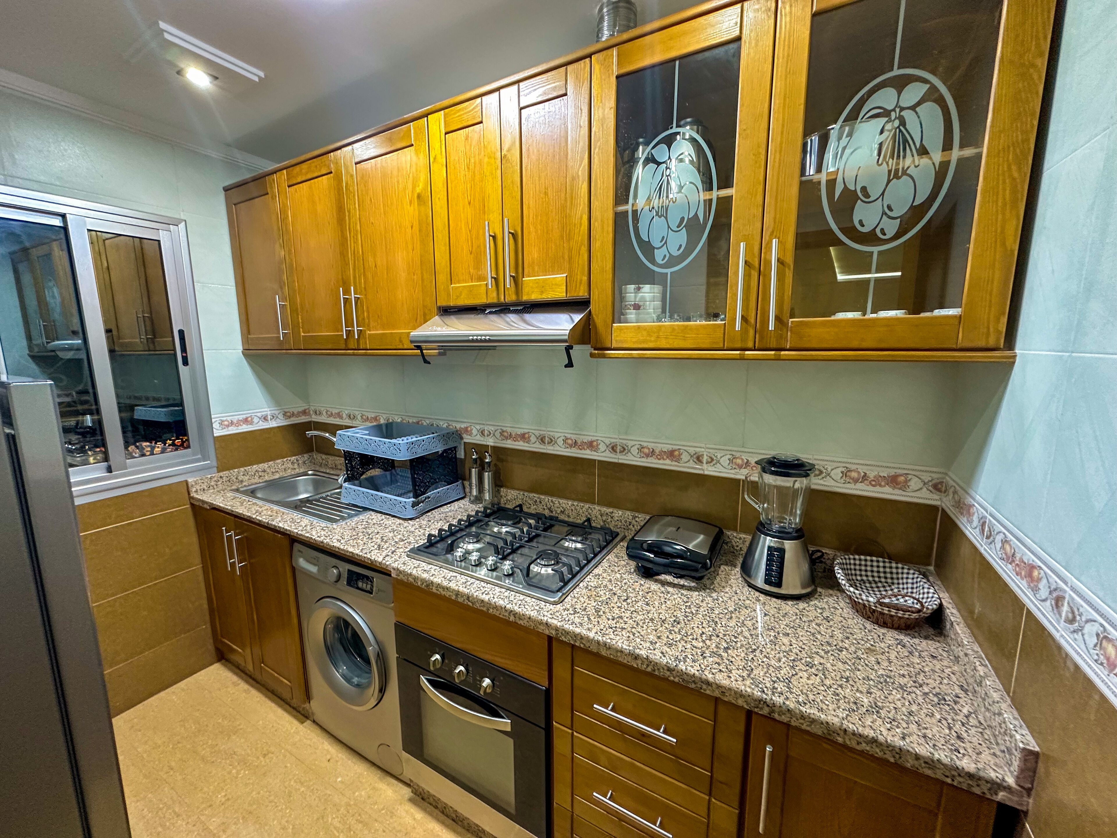 Una cocina con armarios de madera, lavadora, estufa y licuadora.