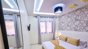 A modern hotel room with a large bed, a bedside table, a mirror, and a ceiling light fixture. - Elite Holiday Homes - Luxury & Centric Flat (Tangier)