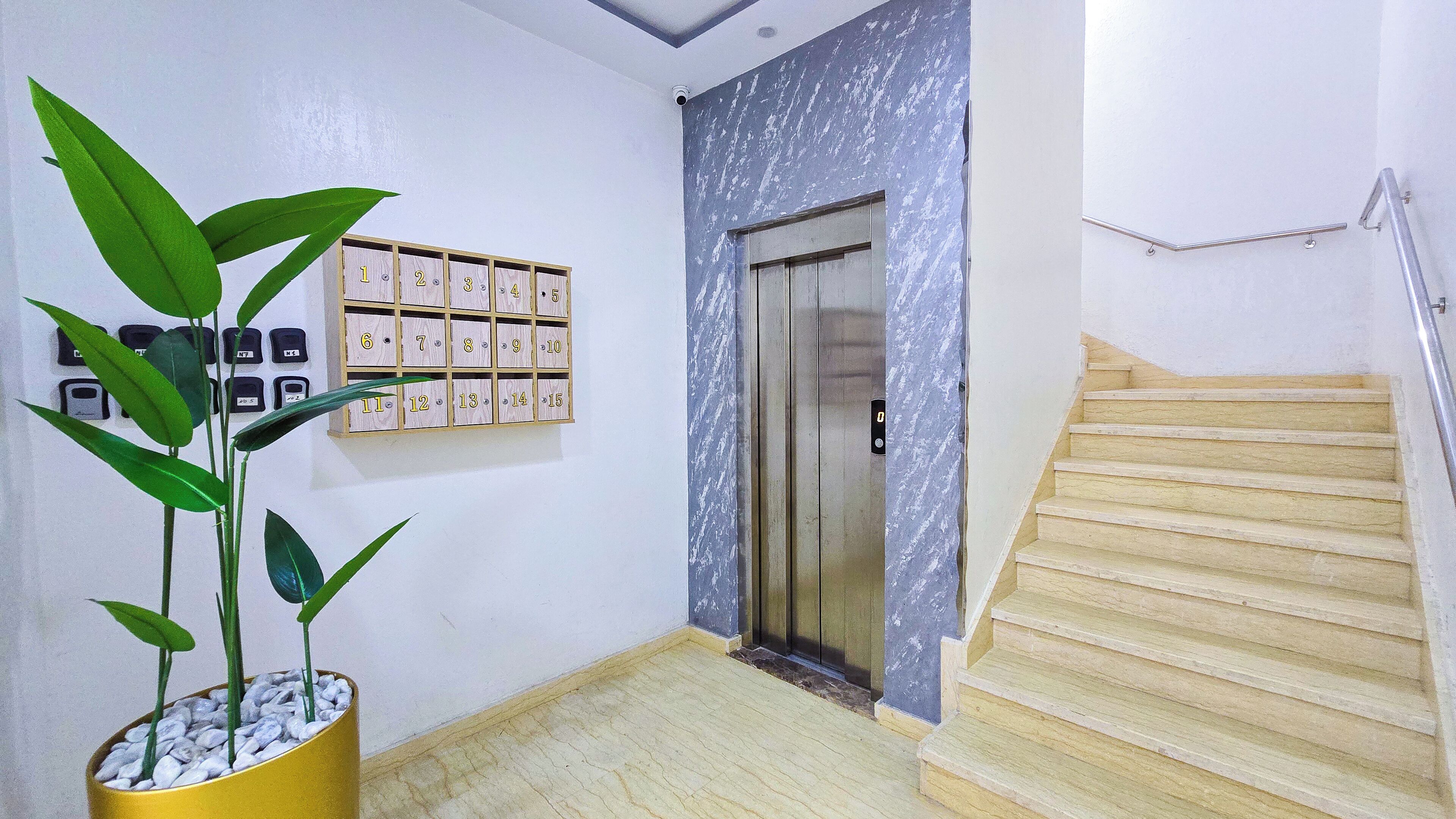 A hallway with a potted plant, a wall-mounted calendar, an elevator, and a staircase.