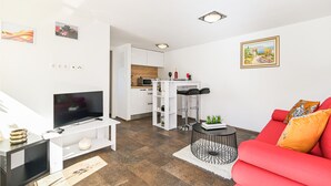 Ein modernes Wohnzimmer mit einem roten Sofa, einem Fernseher und einer Küche im Hintergrund.