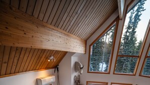 Una sala de estar acogedora con chimenea, un televisor montado en la pared y ventanas amplias con vistas al exterior.