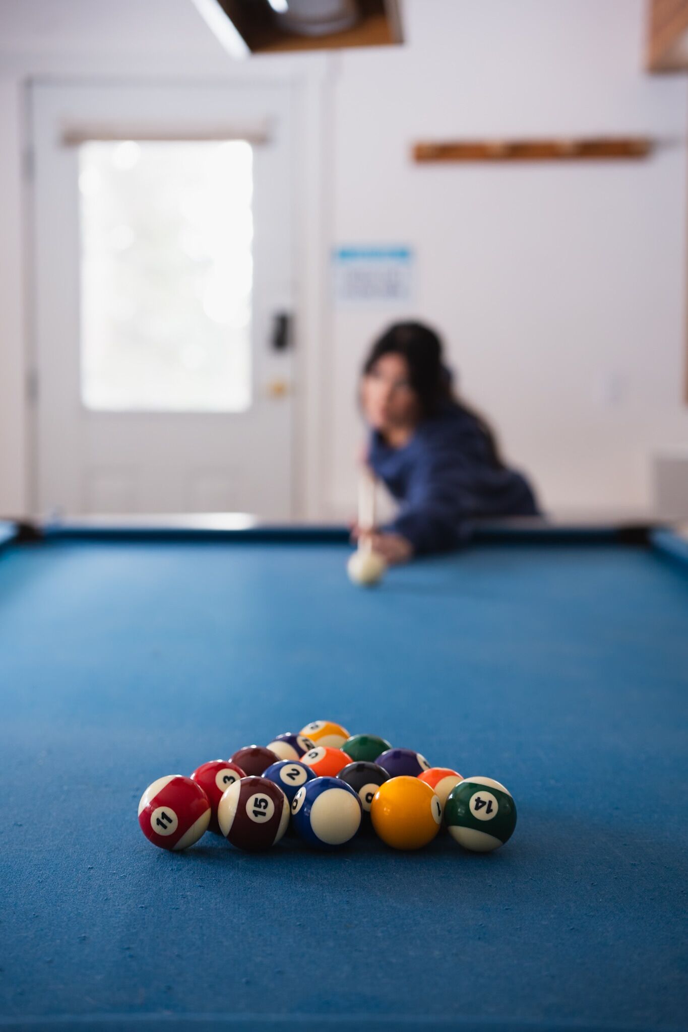 A pool table with billiard balls in a room with a door and a window.