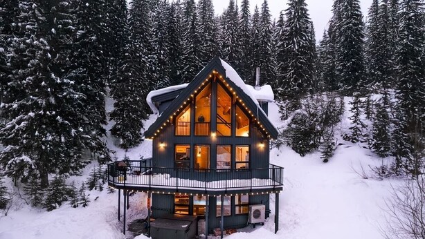 Una cabaña con balcón, rodeada de árboles cubiertos de nieve.