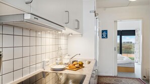 Une cuisine moderne avec des armoires blanches, un évier en acier inoxydable et une vue sur l’extérieur par une porte.