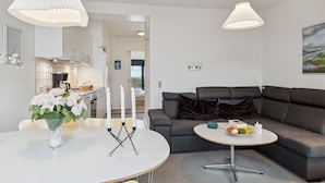Un salon moderne avec un canapé gris, une table basse ronde ornée de fruits et une table à manger blanche décorée de bougies.
