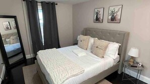 Ein ordentlich eingerichtetes Schlafzimmer mit einem großen Bett, einem Nachttisch mit Lampe und zwei gerahmten Bildern an der Wand.