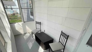 Ein kleiner, abgeschlossener Balkon mit Tisch und zwei Stühlen, einem Fenster und einer Fußmatte mit Schrift.