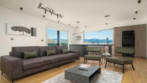 Un salon moderne avec un canapé gris, une table basse et une vue sur les montagnes grâce à de grandes fenêtres.