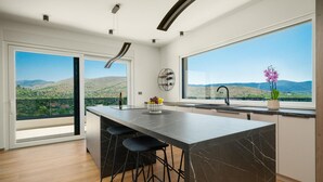 Une cuisine moderne dotée d’un îlot en marbre, de tabourets de bar et offrant une vue sur un paysage montagneux.