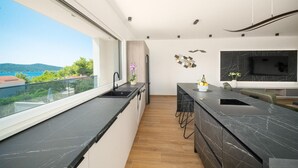 Une cuisine moderne dotée d’une grande fenêtre, d’un plan de travail en marbre noir et offrant une vue sur la mer.