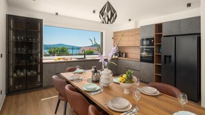Une cuisine moderne avec un coin repas, de grandes fenêtres et une vue sur l’extérieur.