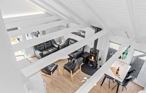 Un espace de vie moderne de style loft, avec un plafond haut, des poutres apparentes en bois, un canapé en cuir noir, une table à manger en bois et un poêle à bois.