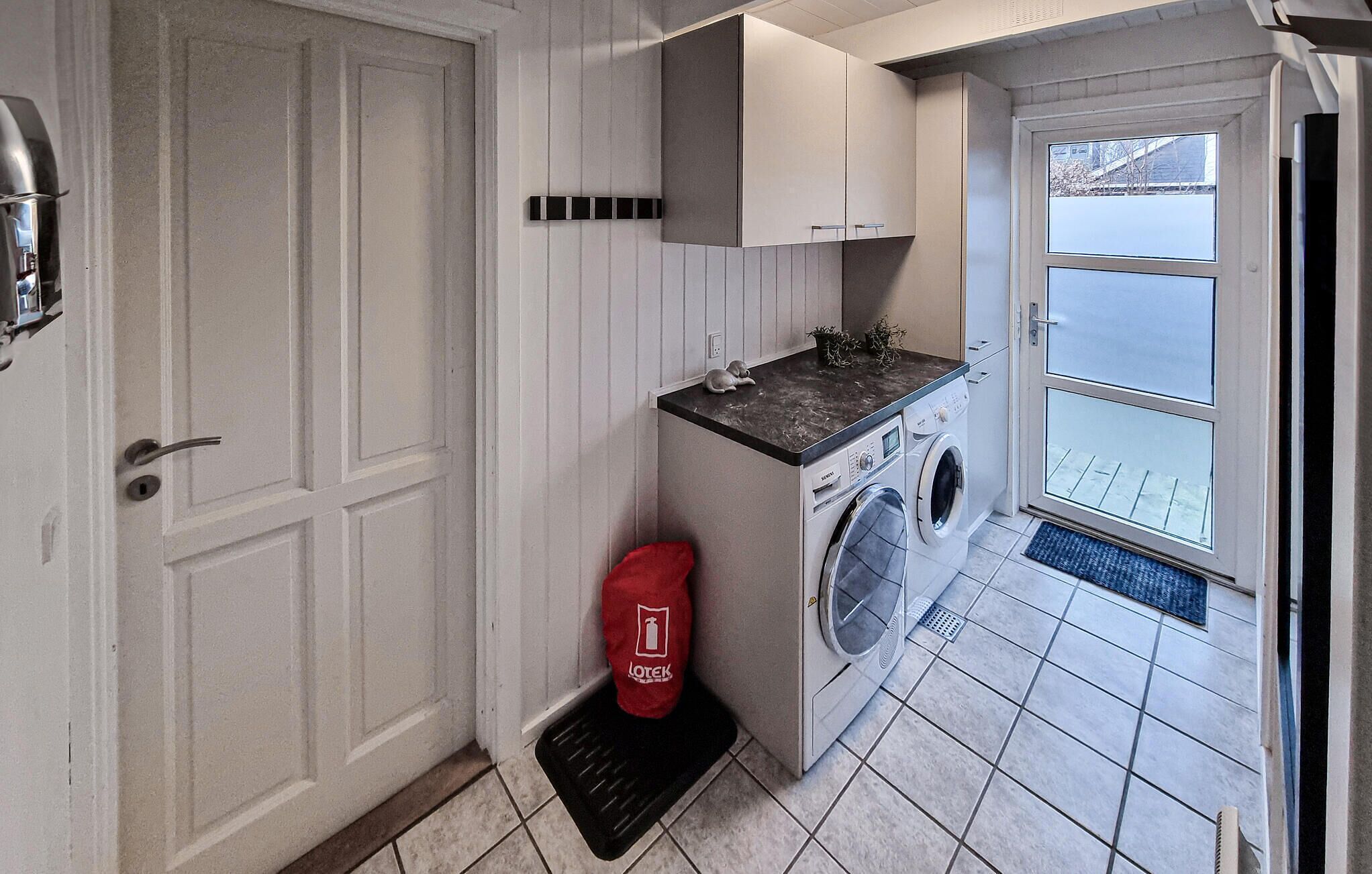 Une petite buanderie comprenant un lave-linge, un petit évier et un sac à linge rouge.
