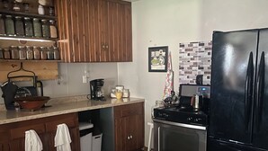 Eine Küche mit Holzschränken, einem schwarzen Kühlschrank, einem Herd und einer Kaffeemaschine.