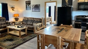 Un salon rustique avec une table à manger en bois, des canapés et une tête de cerf accrochée au mur.