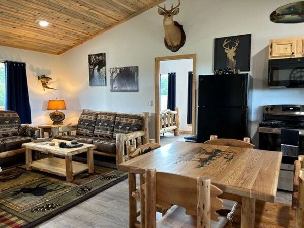 A rustic living room with a wooden dining table, sofas, and a mounted deer head. - 3 mins. to Jasper, AR/less than 3 mi. to Hasty cutoff access for Buffalo River! (Jasper)