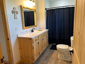 A bathroom with wooden cabinets, a white sink, a mirror, a black shower curtain, and a white toilet. - 3 mins. to Jasper, AR/less than 3 mi. to Hasty cutoff access for Buffalo River! (Jasper)