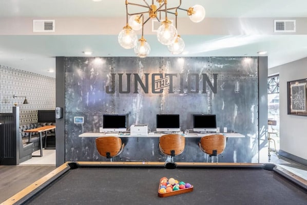 A reception area with a 'JUNCTION' sign, three computer stations, a pool table with balls, and a modern chandelier.