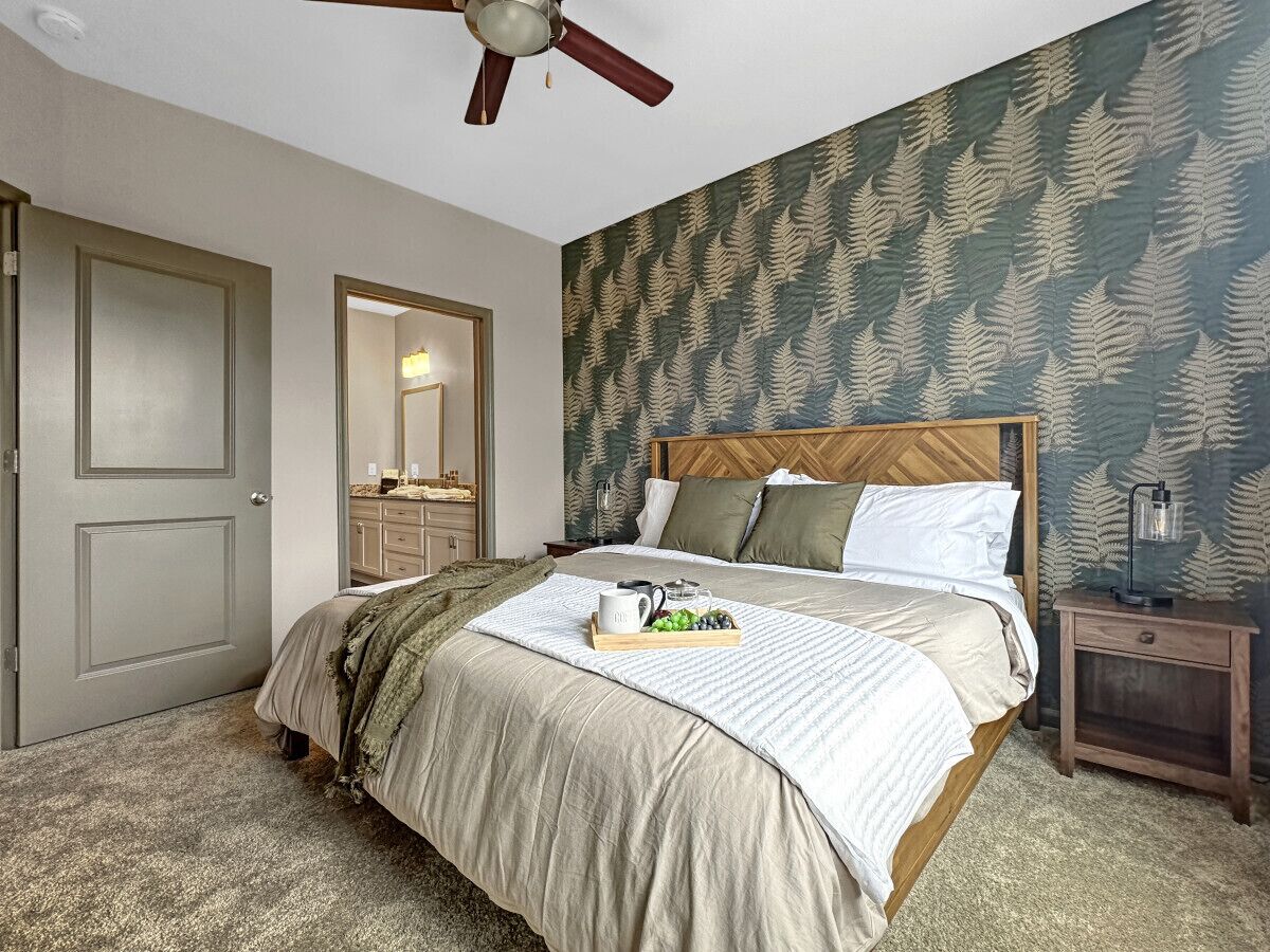 Une chambre à coucher avec un lit, une table de chevet, un ventilateur de plafond, une porte et un miroir.