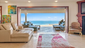 Una sala de estar con vista al océano, un sofá color beige, un sillón de mimbre y una alfombra.