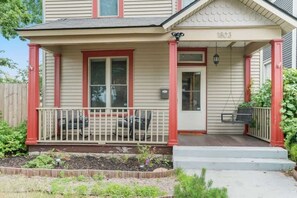 A two-story house with a porch, a front door, and a small garden area.