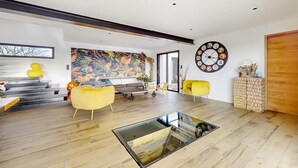 Ein modernes Wohnzimmer mit einem Glastisch, gelben Sesseln, einem farbenfrohen abstrakten Gemälde und einer runden Wanduhr.