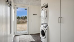 Een wasserette met een wasmachine en droger, een deur naar buiten en een kleed op de vloer.