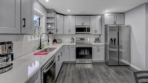 A modern kitchen with grey cabinets, stainless steel appliances, and a wooden floor. - Pocono Paradise: Spacious Fun for the Whole Family (Long Pond)