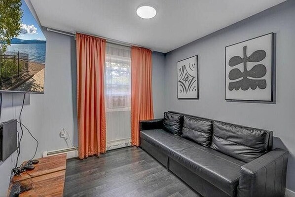 A modern living room with a leather sofa, orange curtains, and two abstract wall art pieces. - Pocono Paradise: Spacious Fun for the Whole Family (Long Pond)