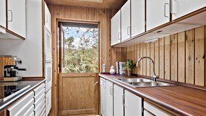 Cocina compacta con armarios de madera, un lavamanos integrado y una cafetera.