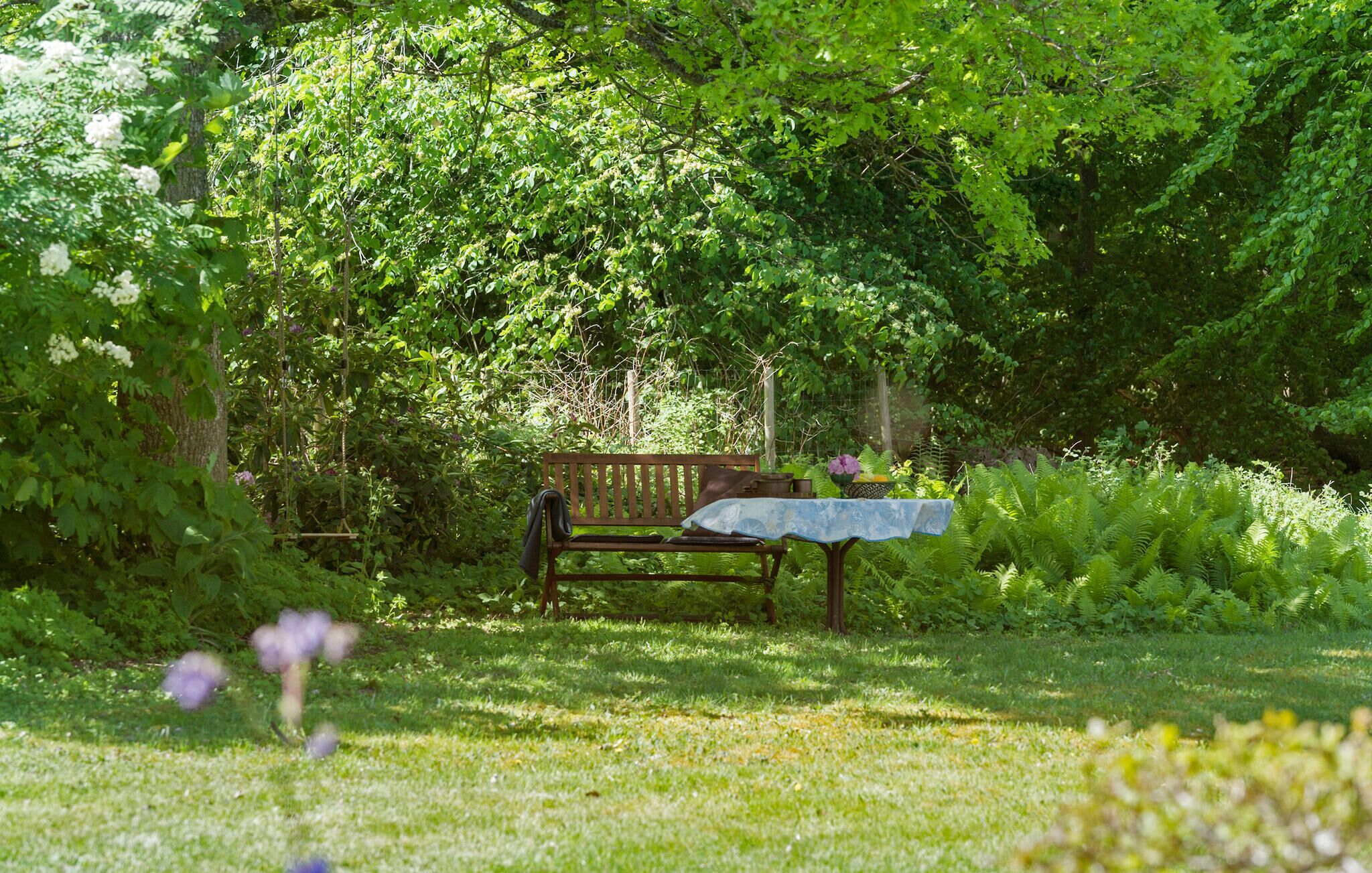 A wooden bench with a table in a lush garden setting.