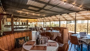Un restaurante con techos altos, luces colgantes y vistas al exterior. Las mesas están dispuestas con cubiertos y servilletas.
