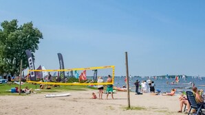 Una cancha de voleibol de playa con red, rodeada de gente y bañistas.