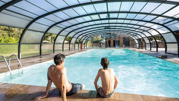 Una piscina interior con techo de cristal y solárium de madera.