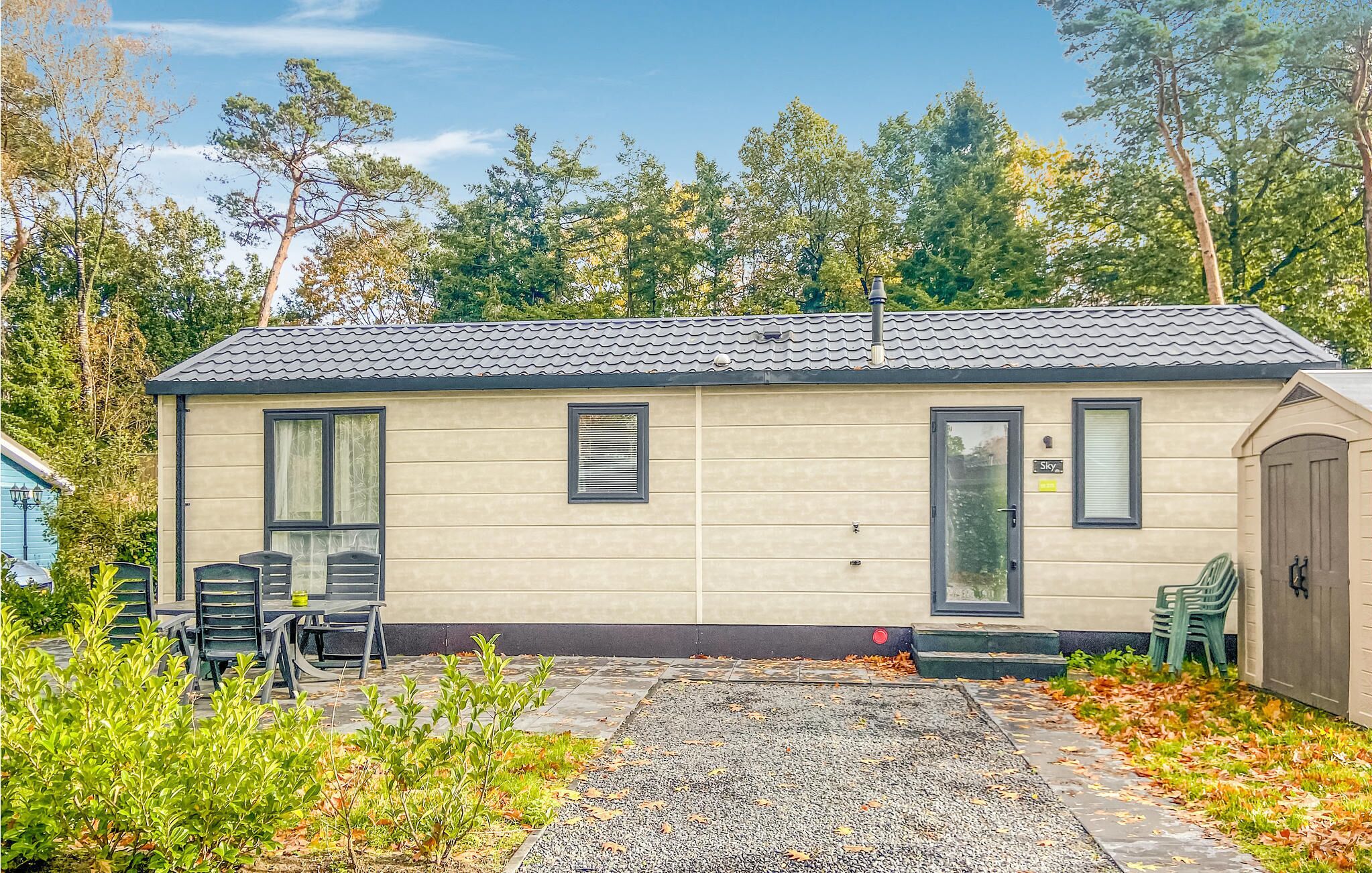 A single-story mobile home with a tiled roof, a front door, and a small porch area with chairs.