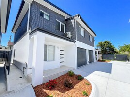 A modern two-story house with a garage, a front door, and a small garden area with red flowers.