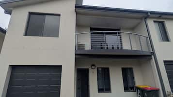 A two-story building with a garage, a balcony, and a small garden area.