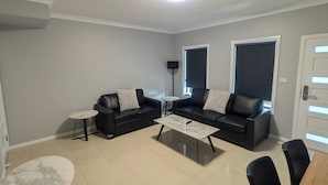 Una sala moderna con dos sofás de cuero negro, una mesa de centro blanca, una mesita redonda y una mesa de comedor con sillas.