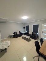 A modern living room with two black leather sofas, a white coffee table, a small round table, and a dining table with chairs.