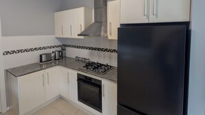 Una cocina con armarios blancos, un refrigerador negro, una estufa a gas y un salpicadero de azulejos.