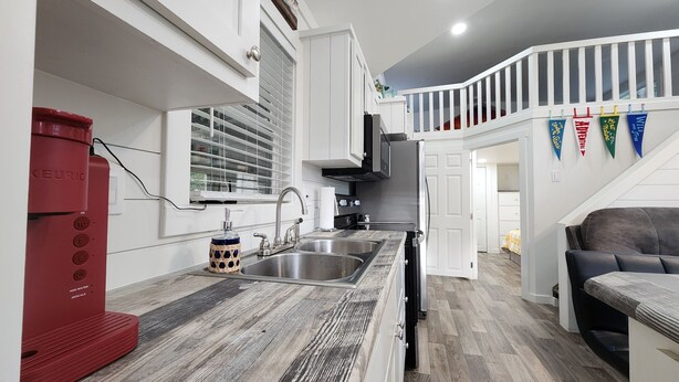 A modern kitchen with white cabinetry, a red coffee maker, a built-in oven, and a wooden countertop.