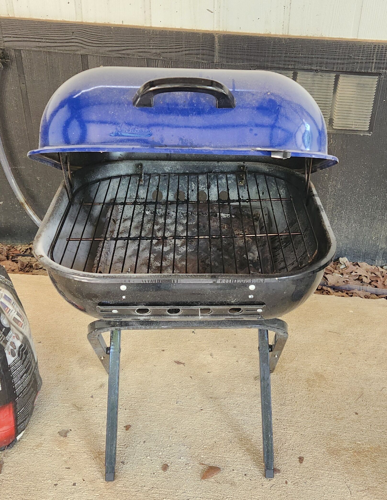 A portable grill with a blue lid, a metal grate, and a stand.