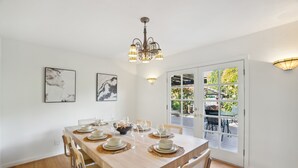 Un comedor con una mesa de madera dispuesta para cuatro personas, sillas, una araña y dos lámparas de pared.