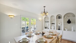 Un comedor con una larga mesa dispuesta para una comida, paredes blancas y un candelabro.