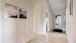 Pasillo interior de madera con una cita inspiradora enmarcada, vista a una habitación con puerta de vidrio y piso de madera.