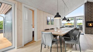 Un comedor moderno con una mesa de madera y sillas grises tapizadas, grandes lámparas colgantes y una chimenea de ladrillo.