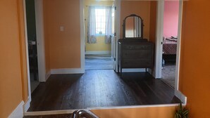 Een kamer met een houten vloer, een dressoir met spiegel en een bed met een gewatteerde spreideken.