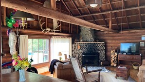 Interior rústico de una cabaña con chimenea de piedra, muebles de madera y una televisión.