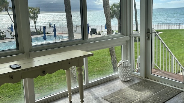 Une pièce dotée d’une grande fenêtre donnant sur une plage, d’une table en bois et d’une vue sur l’océan.